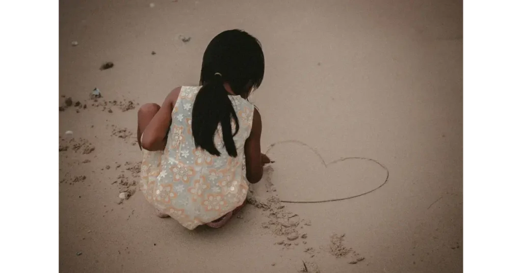 Girl drawing heart in the sand