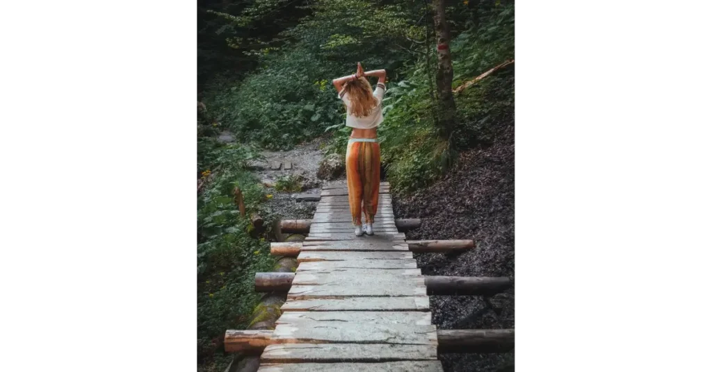 Woman standing on a wooden pathway in the woods with thankful gesture